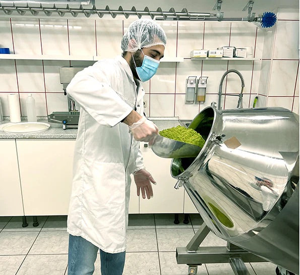 Mitarbeiter in Schutzkleidung füllt grünes Matcha-Pulver in eine Edelstahl-Trommel in der Matchatto-Manufaktur
