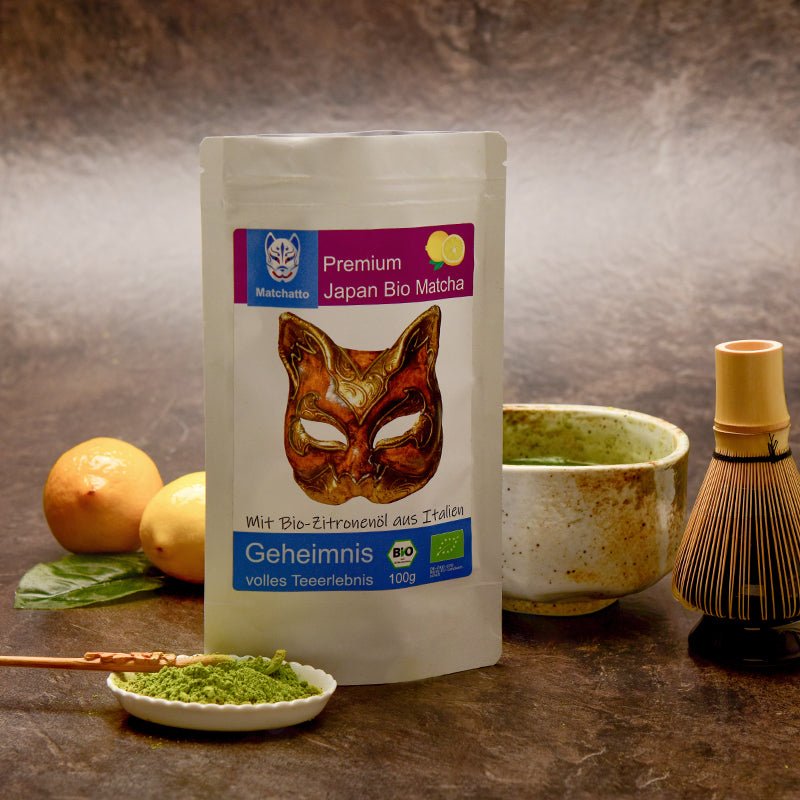 Matchatto Bio-Matcha mit Zitronenöl in 100g-Packung, daneben Chasen, Matcha-Schale, Zitronenfrüchte und Pulver auf Löffel – stilvoll arrangiert auf dunklem Naturhintergrund.