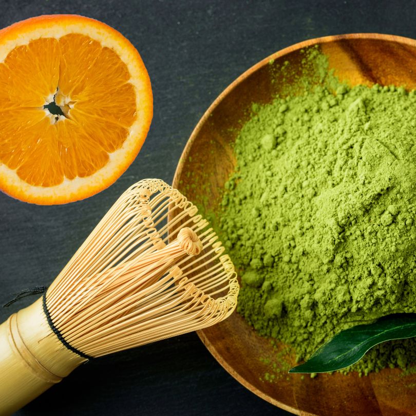 Matcha Latte Pulver mit Matcha-Besen und Orangenscheibe