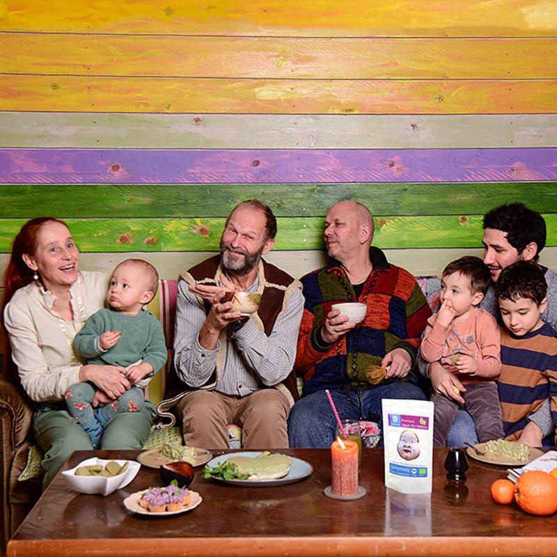 Zufriedene Familie am Tisch mit Matcha-Tassen, im Vordergrund ein Matchatto Bio-Matcha-Beutel – gemeinsamer Teegenuss in entspannter Atmosphäre.