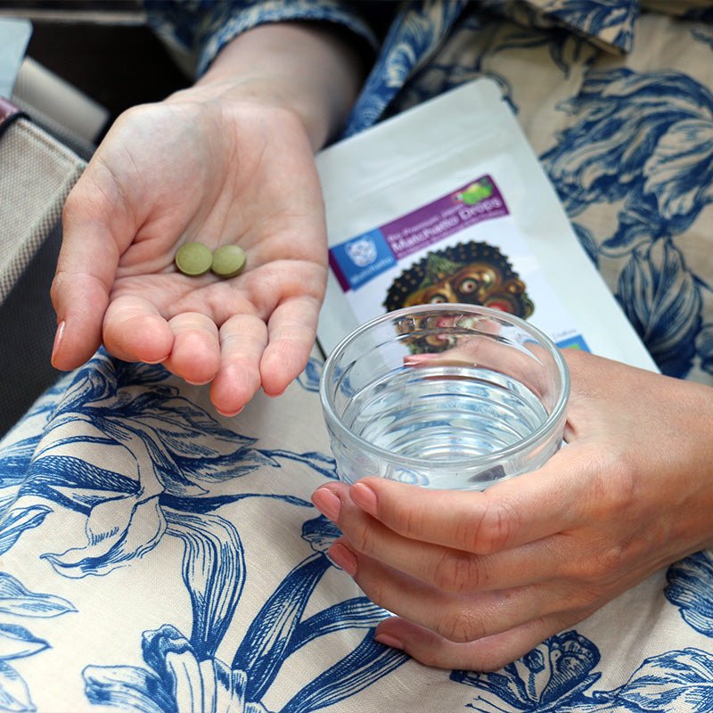 Frau hält Matchatto Bio Matcha Drops und ein Glas Wasser in der Hand – praktische Einnahme unterwegs, Presslingsbeutel mit Guarana-Zitrone im Hintergrund sichtbar.